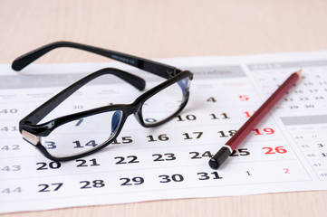 Black glasses and a pencil lie on the calendar