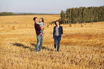 Naklejka na ściany i meble Happy young family with 2 year old girl walking in a harvested field