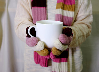 Hand holding warm milk with white sweater, scarf and hand gloves