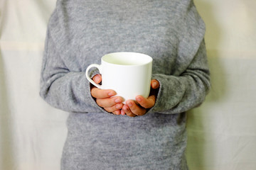 Hand holding warm drink with grey sweater