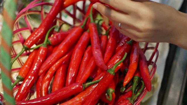 Female hand choosing and holding red chili peppers in a store. Young woman buying healthy food in the blur background of a supermarket