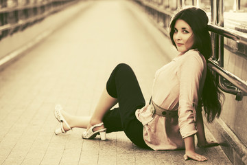 Happy young fashion woman sitting on the sidewalk