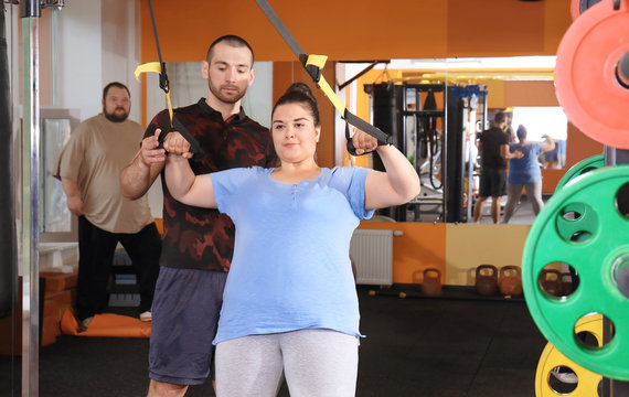 Overweight young woman with trainer in gym