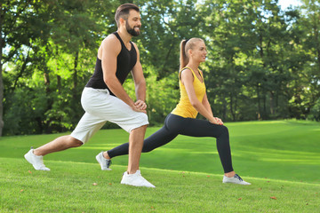 Young sporty couple doing exercise in green park