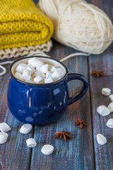 Hot chocolate or cacao in a blue mug with marshmallows on the table with wool