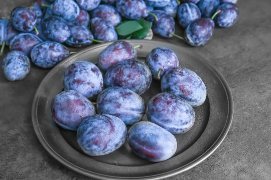 Plate with tasty ripe plums on dark table