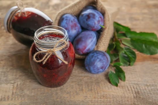 Small sack with ripe plums and tasty jam in jars on wooden table