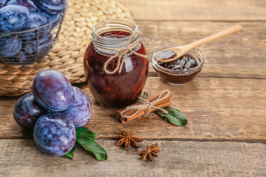Composition with ripe plums and delicious jam on wooden background
