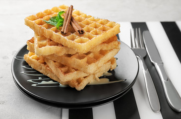 Plate with delicious cinnamon waffles on table