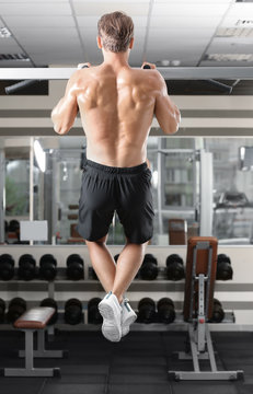 Sporty young man doing pull ups in gym