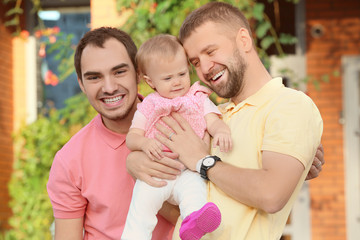 Male gay couple with adopted baby girl, outdoors