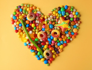 Colorful candies arranged as heart on yellow background