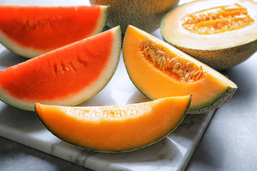 Marble board with slices of fresh melon and watermelon on table, closeup