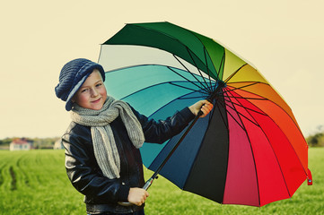 The child, standing under a colored umbrella on the green meadow .Retro style