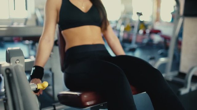 Young beautiful girl brunette with long hair doing exercises for legs muscles in gym. 4 k