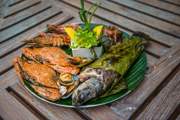Dish of mixed grilled seafood including, fish, crab, mussel, shrimp, squid on wooden table