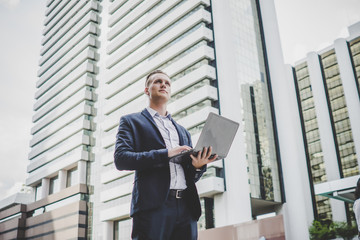 Fototapeta premium Handsome businessman standing on the way to office with laptop in hand.