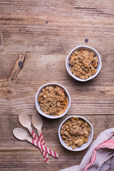 Apple crumble served in individual white ramekins placed on top of a cotton dishtowel. Rustic wood background. Copy space. 