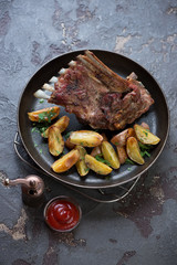 Roasted lamb meat with potato wedges served on a metal plate, high angle view