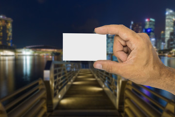 Hand holding business card with blank with city by night in background