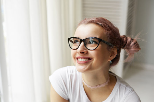 Headshot of adorable cute young Caucasian female in big eyewear and choker necklace smiling broadly, showing her perfect straight teeth, feeling happy and excited while making plans for weekend