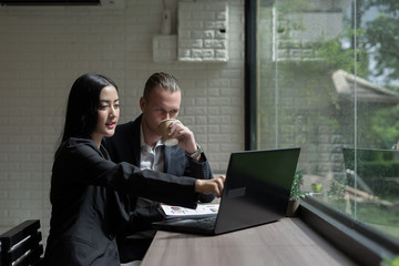 Young business woman showing something to mature businessman seen on her laptop.