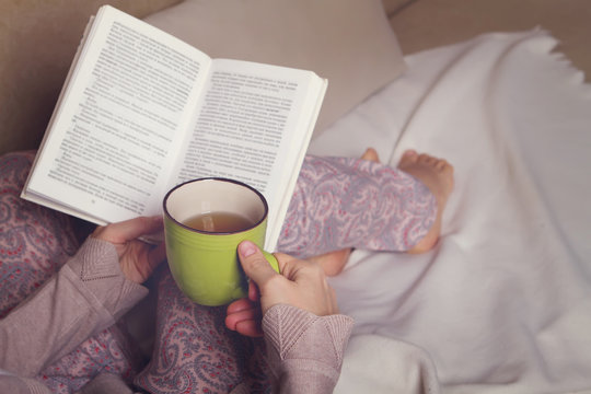 Woman sitting on the sofa reading a book holding her tea mug