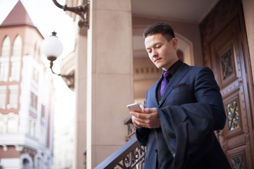 A handsome guy in a suit comes out of the house and calls a taxi on the application on the phone.