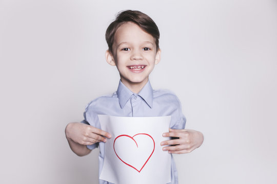 Portrait of young happy smiling brunette boy with picture of heart on the sheet of paper in hands looking at camera isolated.