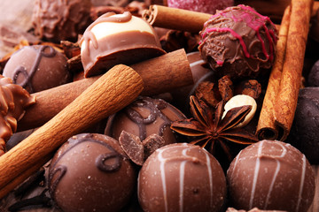 A selection of assorted chocolate truffle pralines on a wooden table with dark chocolate, cinnamon and anise.