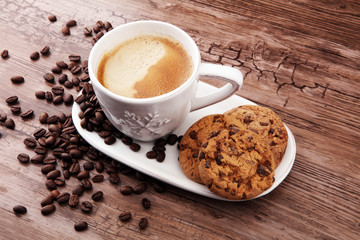 Coffee cup with chocolate cookies and coffee beans on wooden background