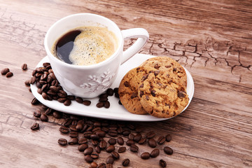 Coffee cup with chocolate cookies and coffee beans on wooden background