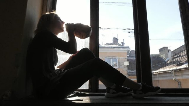 Silhouette of girl drink alcohol, sitting on on the windowsill.