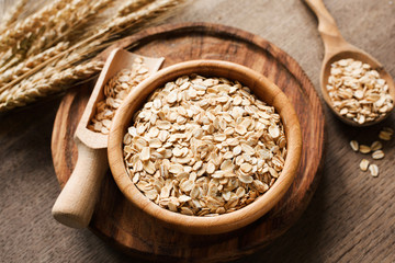 Rolled oats, organic oat flakes in wooden bowl and golden wheat ears on wooden background. Healthy lifestyle, healthy eating, vegan food concept