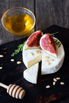 Camembert cheese with fresh figs, honey and pine nuts on dark wooden cutting board. Closeup view