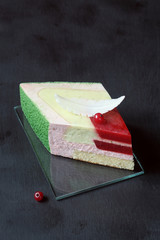 Piece of Contemporary Strawberry Basil Lime Mousse Cake decorated with  White Chocolate Feather, on black background. 