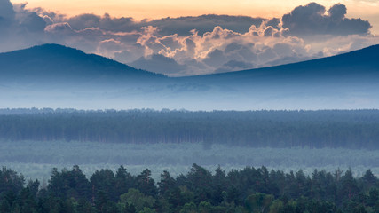 Dramatic sunrise in the mountains with thick evergreen forest in foreground covered with fog, Altai Mountains, Kazakhstan