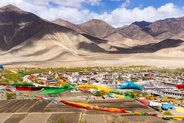 Top view of Samye monastery, with prayer flags in foreground and himalaya range in background -...