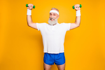 Body care, hobby, weight loss lifestyle. Cheerful cool grandpa with humor grimace exercising holding equipment up, lifts it with strength and power, wearing blue sexy shorts, so hot!