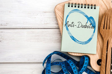 Notepad with Anti-Diabetes on chopping board with wooden fork and spoon and the measuring tape on the white table , Diabetes world day on 14 November encourage awareness campaign background concept