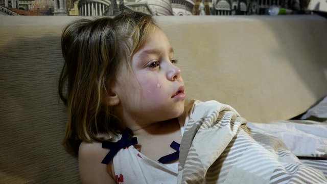 4K footage. A frustrated, tear-stained child in bed. Girl 4-5 years of European appearance. She has tears in her eyes.
