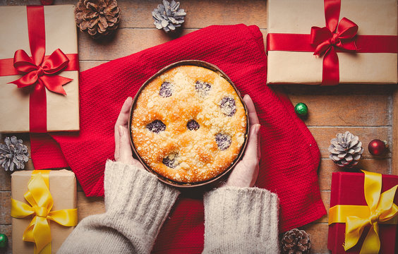 Female hands holding Christmas pie with gifts around