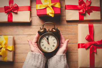 Woman hands holding alarm clock with Christmas gifts