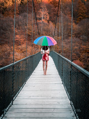 Beautiful Caucasian European girl with a red skirt, high boots and white top on a bridge holding a colorful rainbow umbrella