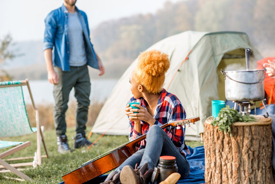 Multi ethnic couple of friends dressed casually talking during the outdoor recreation with tent near the lake