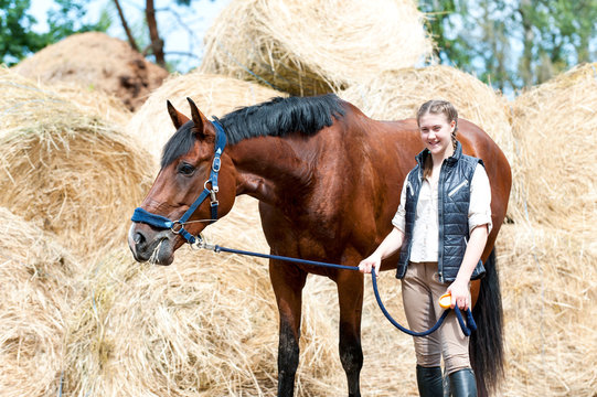 Young teenage cheerful owner girl leads beautiful brown horse