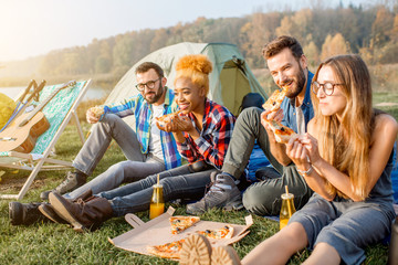 Multi ethnic group of firends dressed casually having fun eating pizza during the outdoor...