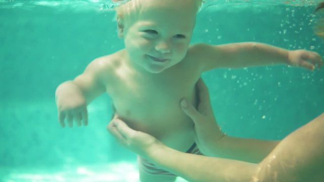 Adorable toddler is swimming under the water in the swimming pool together with his mother. An underwater shot. Slowmotion