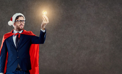 A businessman in a superhero santa costume with a light bulb in his hand on a background of space for text.