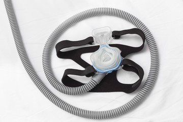 CPAP headgear mask, connecting with strap and hose laying on a bed, for helping people with respiratory problem